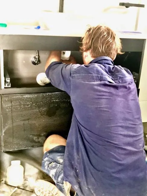 Plumber working under vanity cabinet in Gladstone